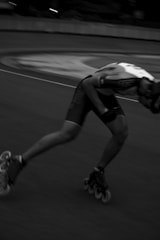A person on inline skates is captured in motion, leaning forward with one leg extended behind. The image is in black and white, emphasizing the motion blur, which conveys a sense of speed.