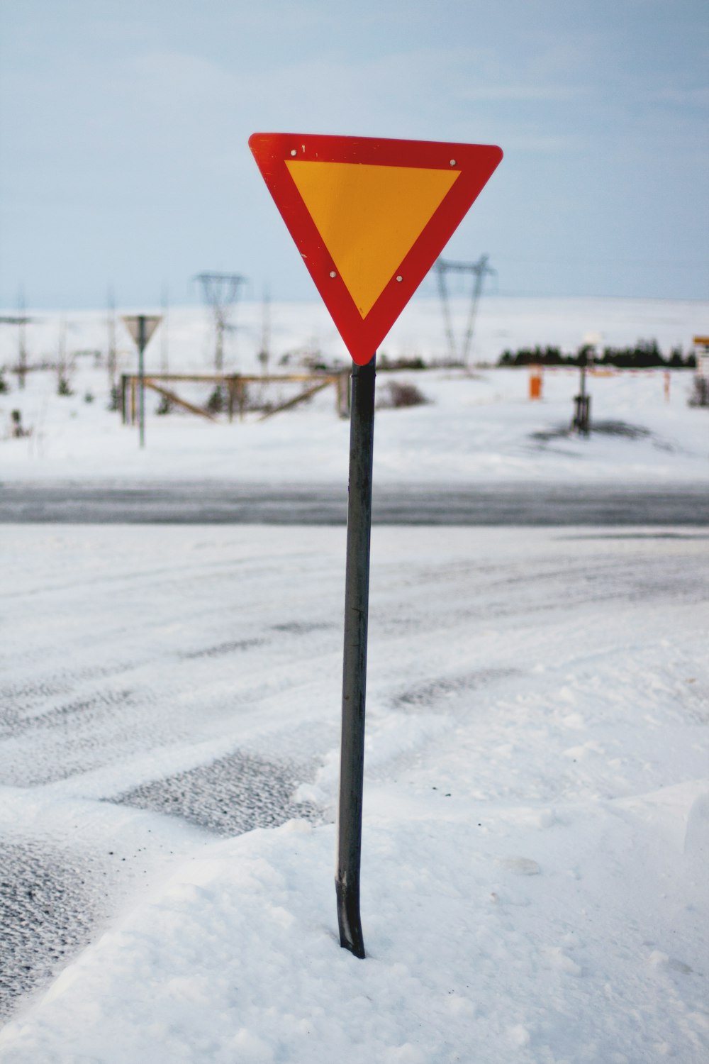triangle road sign beside road covered with snow