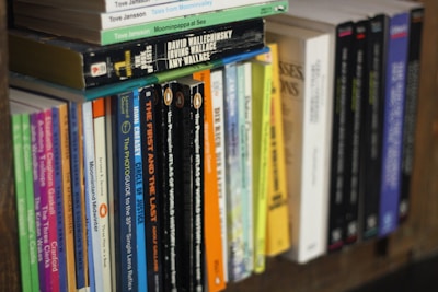 A bookshelf filled with a variety of books standing upright, displaying colorful spines and diverse titles. The focus is on a section of the shelf, showing various genres and authors.