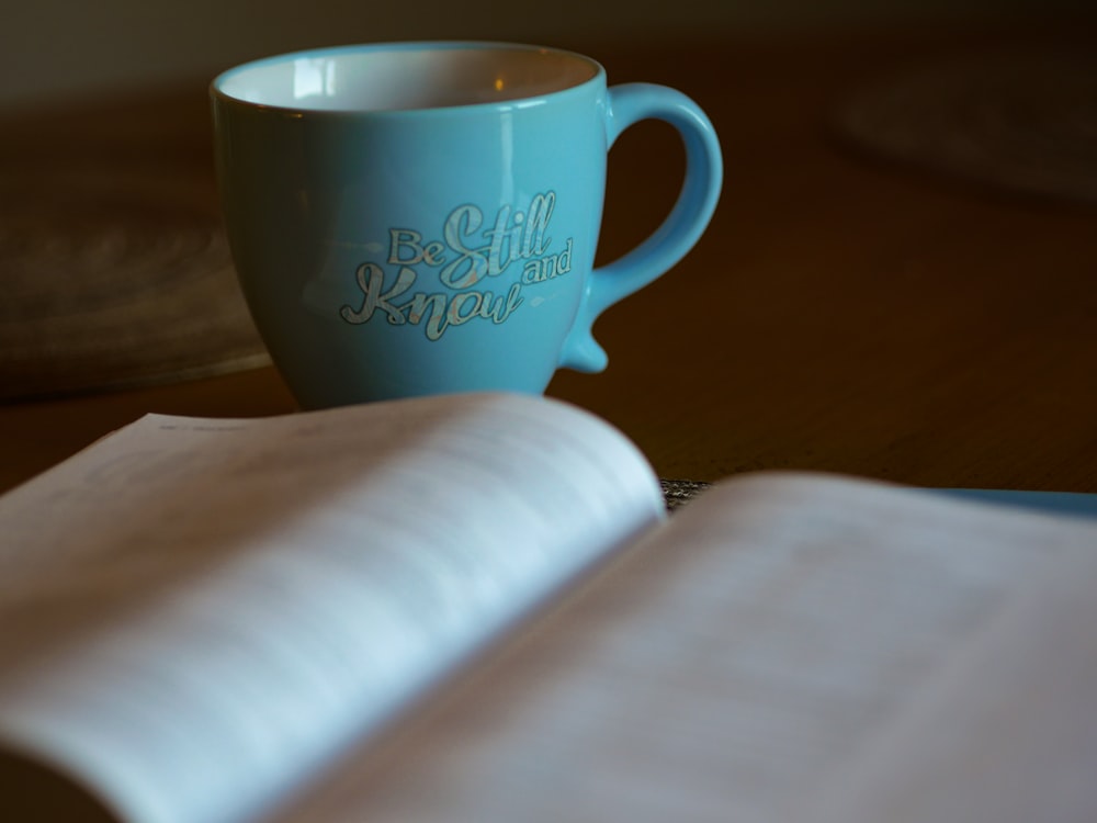 Fotografía de enfoque superficial de libro abierto junto a taza de cerámica azul