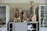 Two anatomical models displaying the human torso are positioned on a cabinet. Cabinets on either side hold various medical supplies and material, with some shelves visible through glass doors. Loose anatomical parts, including a heart and sections of the torso, are scattered around.