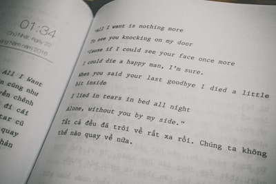 The image features an open book displaying text in two columns. The right column consists of a poem or song lyrics in English, expressing themes of longing and sadness. The left column contains text in Vietnamese. The page on the left also shows a timestamp, '01:34,' and a date, referring to Sunday, May 22, 2016.