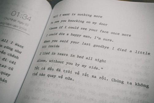 The image features an open book displaying text in two columns. The right column consists of a poem or song lyrics in English, expressing themes of longing and sadness. The left column contains text in Vietnamese. The page on the left also shows a timestamp, '01:34,' and a date, referring to Sunday, May 22, 2016.