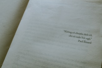 A close-up view of an open book displaying a page with a quote written in Vietnamese. The quote is attributed to Paul Éluard, and the text is printed towards the right side of the page. The page is light beige, giving a vintage or classic feel.