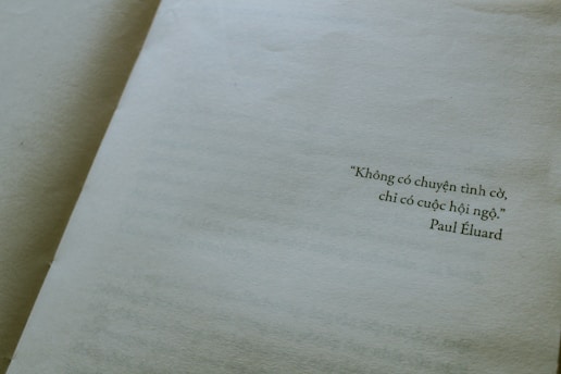 A close-up view of an open book displaying a page with a quote written in Vietnamese. The quote is attributed to Paul Éluard, and the text is printed towards the right side of the page. The page is light beige, giving a vintage or classic feel.