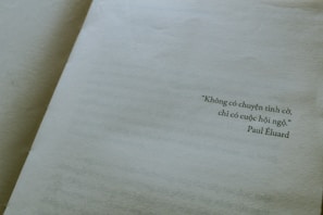 A close-up view of an open book displaying a page with a quote written in Vietnamese. The quote is attributed to Paul Éluard, and the text is printed towards the right side of the page. The page is light beige, giving a vintage or classic feel.