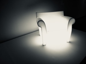 A realistic inflatable doll seated on a modern chair, bathed in soft, warm lighting.