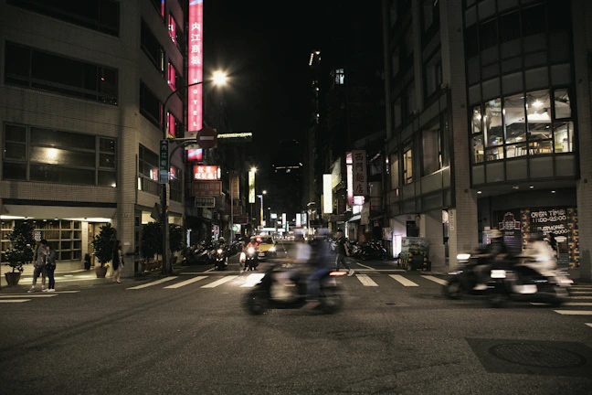 A bustling city street at night, illuminated by colorful neon signs and blurred motion.