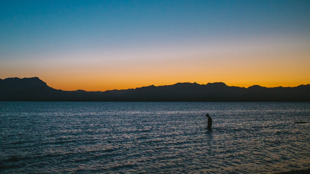 silhouette photo of person on body of water during sunset