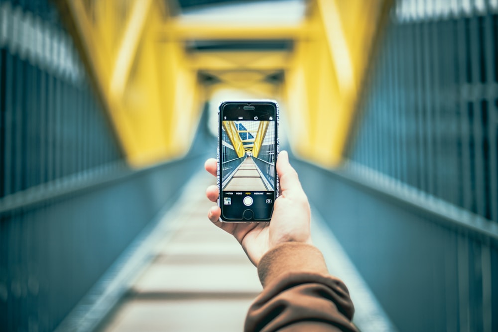 photo de mise au point sélective d’une personne tenant un iPhone 6 gris sidéral prenant une photo d’un pont