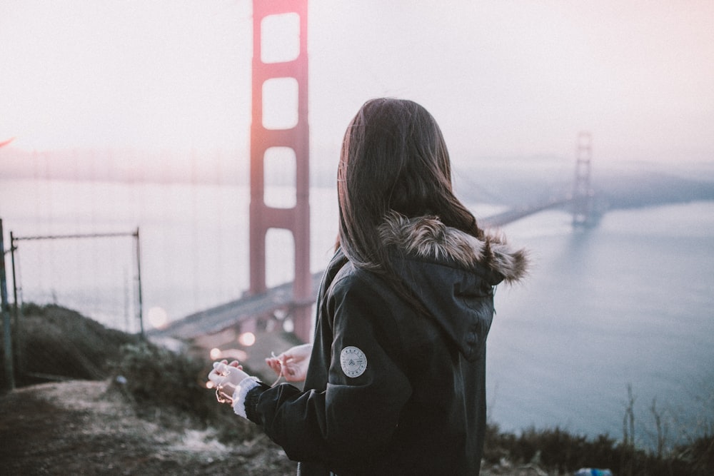 파카 재킷을 입은 여자가 샌프란시스코 다리 근처에 서 있다