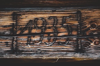 Dark, aged wood with deep engravings that form numbers, giving a rustic and historical feel. The texture of the wood is emphasized by the uneven grain and the contrast between the light and dark areas.