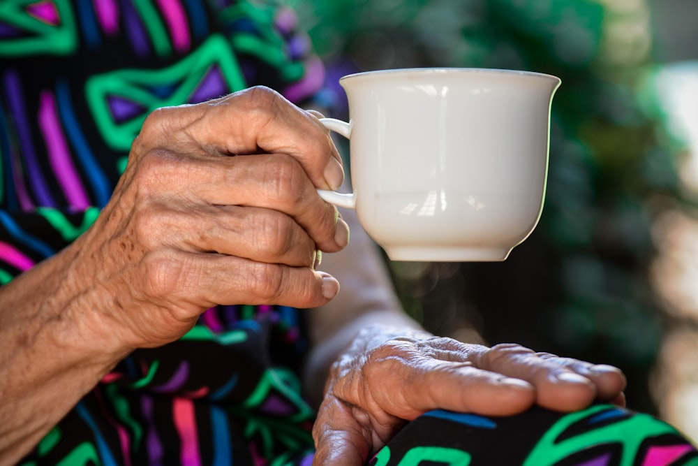 older person holding white ceramic teacup