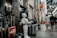 A humanoid robot stands in an indoor shopping arcade next to a display of suitcases. People are walking through the arcade, which is lined with various shops. The area is well-lit, with a mix of natural and artificial lighting. Signs and advertisements in Japanese can be seen around, indicating the prices of products.