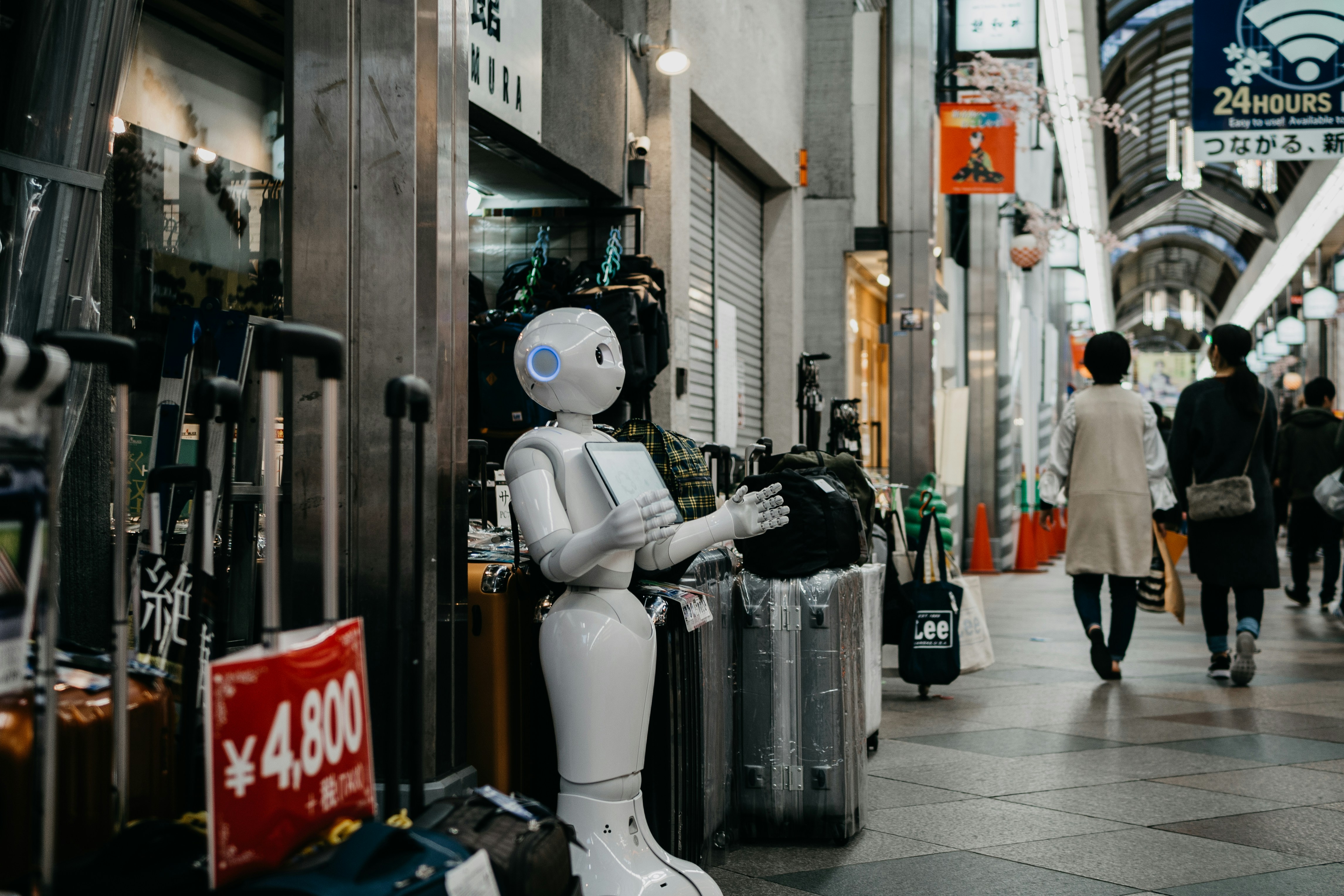 Branimo robot standing beside luggage bags, representing travel and technology.