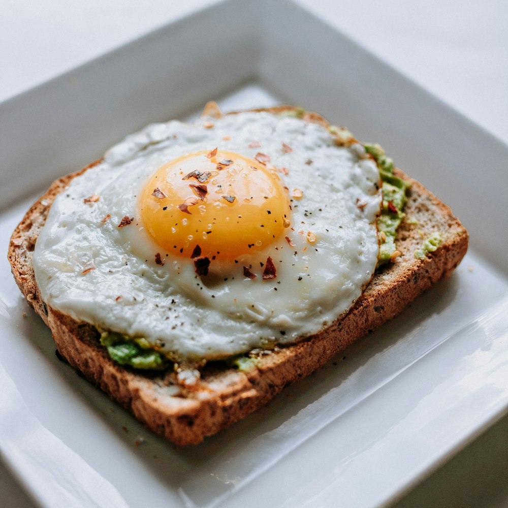 Pain avec œuf au plat servi sur une assiette en céramique blanche