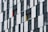 A building facade featuring a grid pattern of alternating dark and light panels. The design incorporates several windows with closed shutters, and two colored panels, one red and one yellow, adding vibrant accents to the structure.
