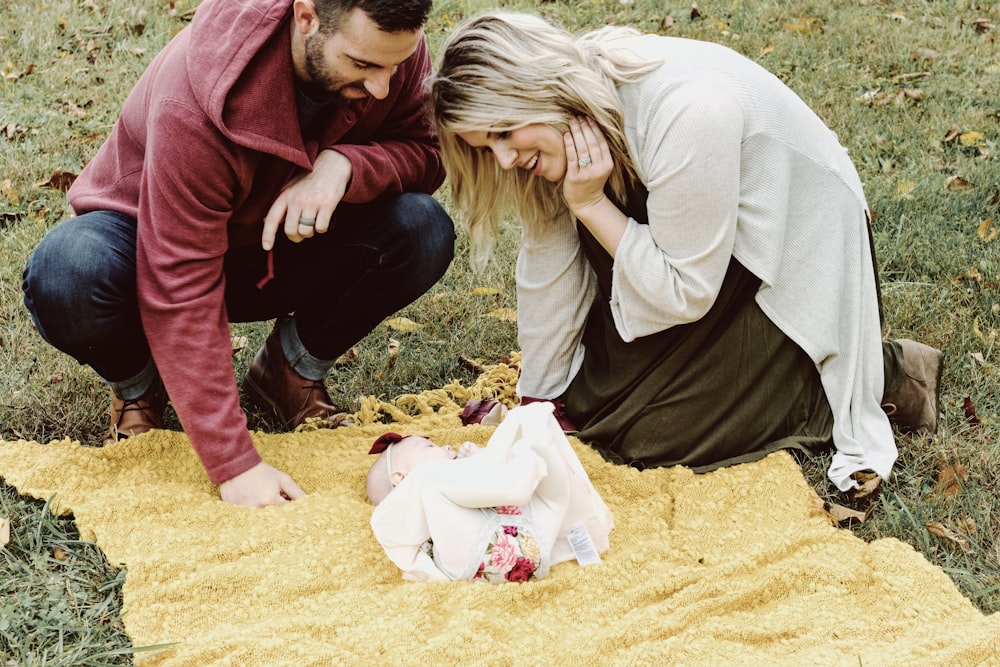 man and woman looking at baby on picnic maty