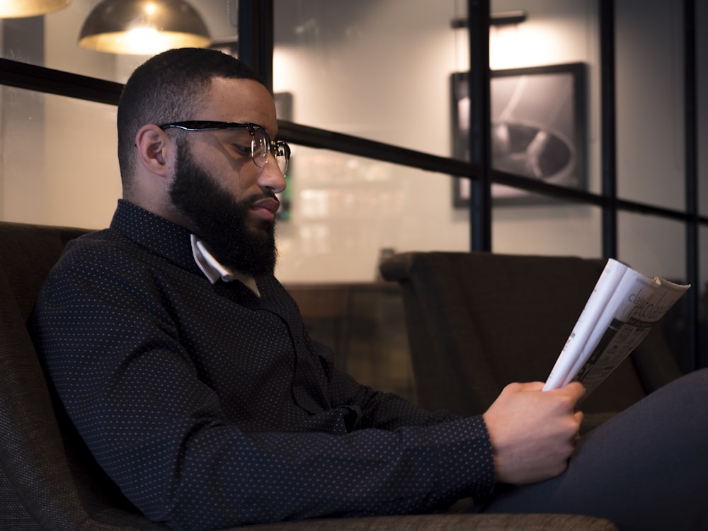 man sitting on sofa while reading book