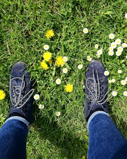 Close-up of hiking boots on a rugged trail with wildflowers blooming nearby.