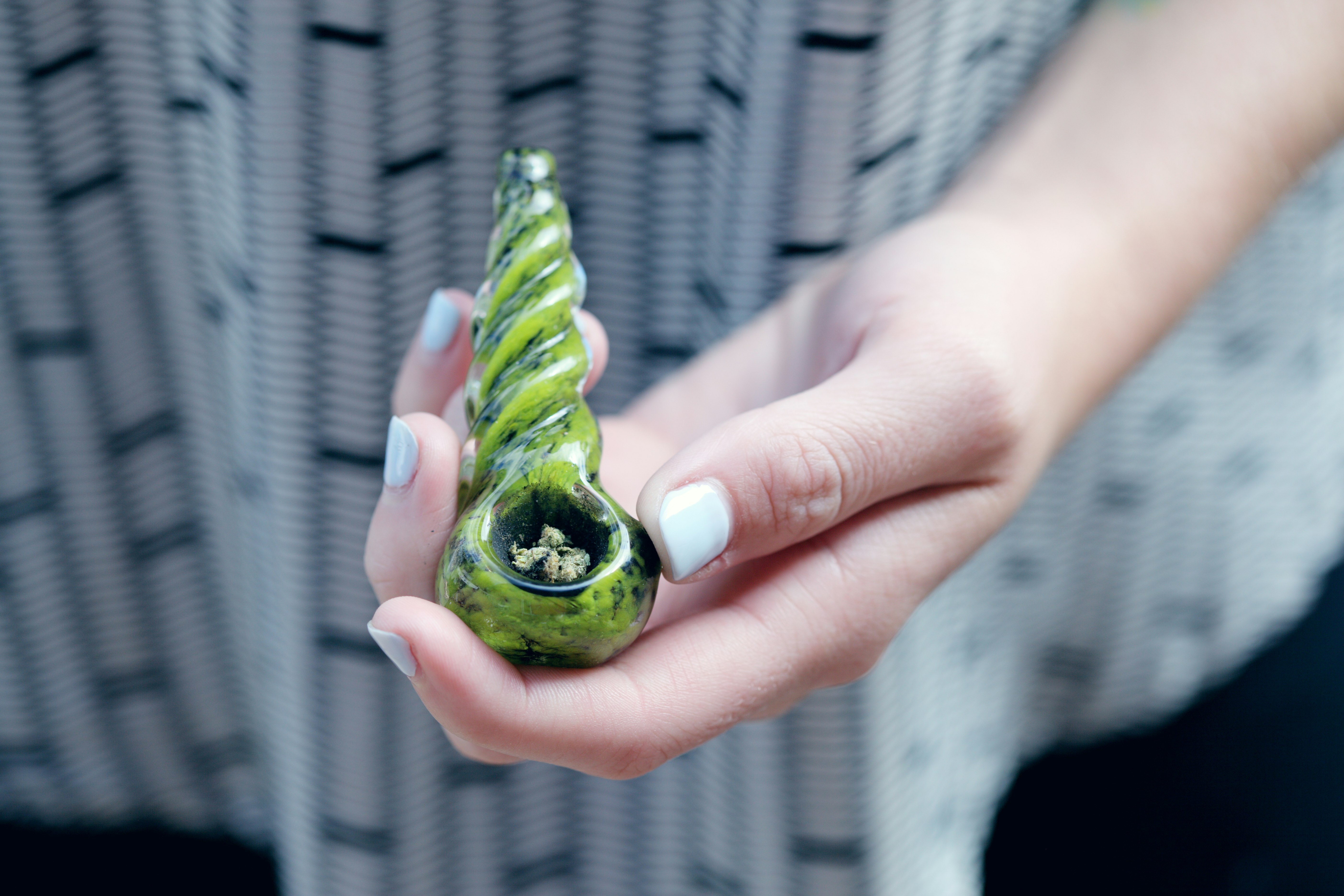 Woman holding a glass cannabis pipe filled with medical grade marijuana.