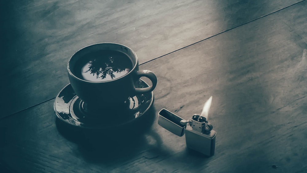 white ceramic tea cup on saucer near gray flip lighter