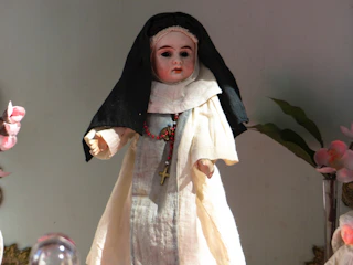 A detailed fofucha doll dressed in a boy's communion outfit, holding a small cross.