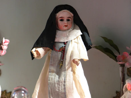 A detailed fofucha doll dressed in a boy's communion outfit, holding a small cross.