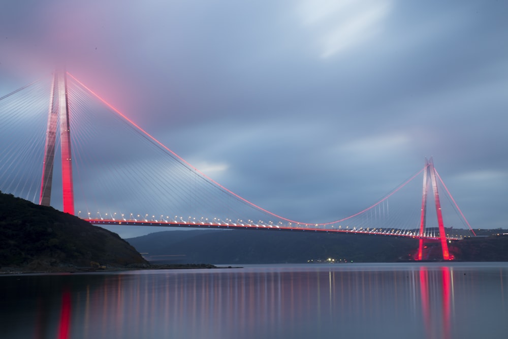 gray concrete bridge with red LED light above calm water