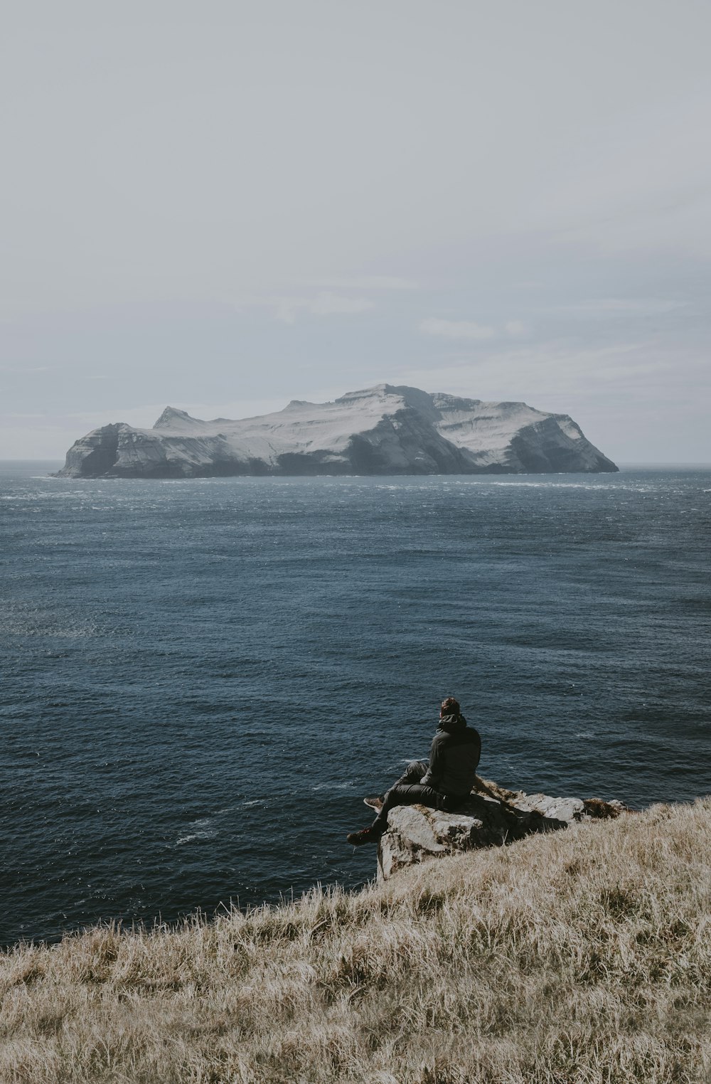 Mann sitzt auf Felsformation am Meer