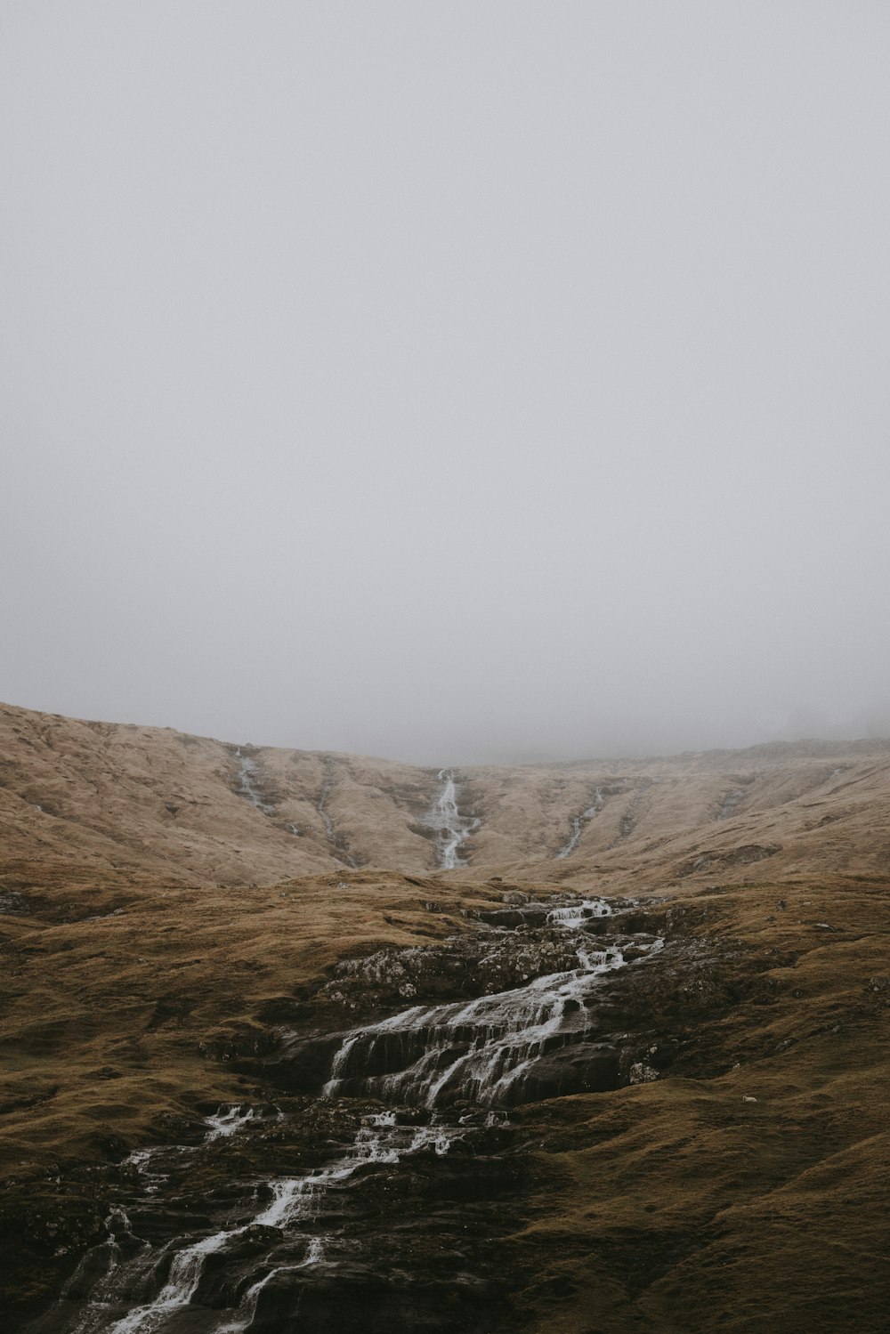 a foggy mountain with a stream running through it
