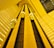 A dynamic perspective looking upward at an interior elevator system with several rounded elevator cars ascending and descending along vertical tracks. The architecture features geometric patterns and a warm yellow lighting that fills the space.