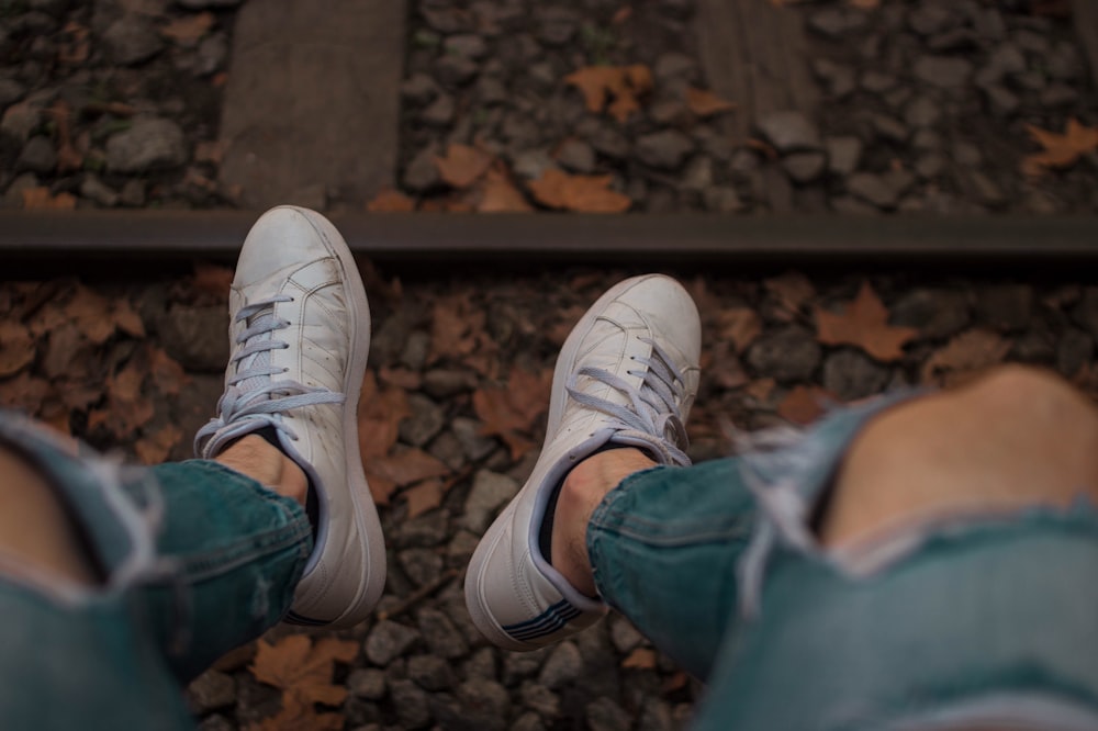 sitting person in front of railway wearing distressed blue fitted jeans and pair of white low-top sneakers