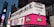 A bustling urban setting with large digital billboards displaying colorful advertisements. Prominent ads include 'Make Google do it' and 'American Idol Winner David Cook'. Bright neon colors and giant screens dominate the scene, hinting at a lively nightlife area.