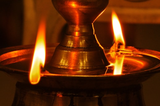 A close-up of a beautifully crafted brass kuthu vilakku glowing softly in warm light.