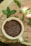 A cream-colored ceramic cup filled with brown flaxseeds rests upon a wooden surface. Surrounding the cup are fresh green mint leaves scattered across the wood, which displays a natural, rustic texture.