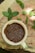 A cream-colored ceramic cup filled with brown flaxseeds rests upon a wooden surface. Surrounding the cup are fresh green mint leaves scattered across the wood, which displays a natural, rustic texture.