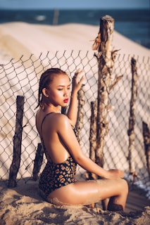 woman wearing monokini sitting on sand holding fence