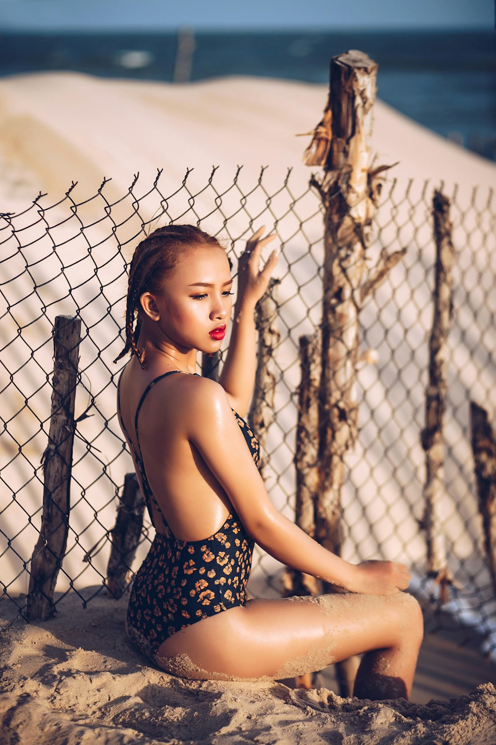 woman wearing monokini sitting on sand holding fence