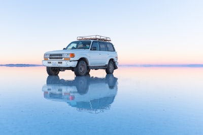 white suv parked on body of water bolivia teams background