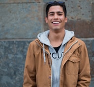 man in brown coat standing near concrete wall smiles