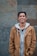man in brown coat standing near concrete wall smiles