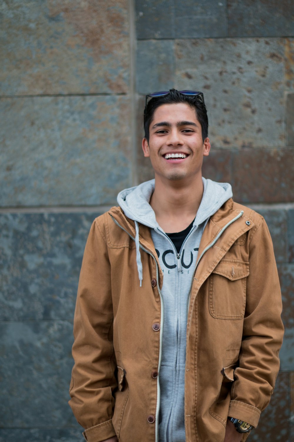 man in brown coat standing near concrete wall smiles