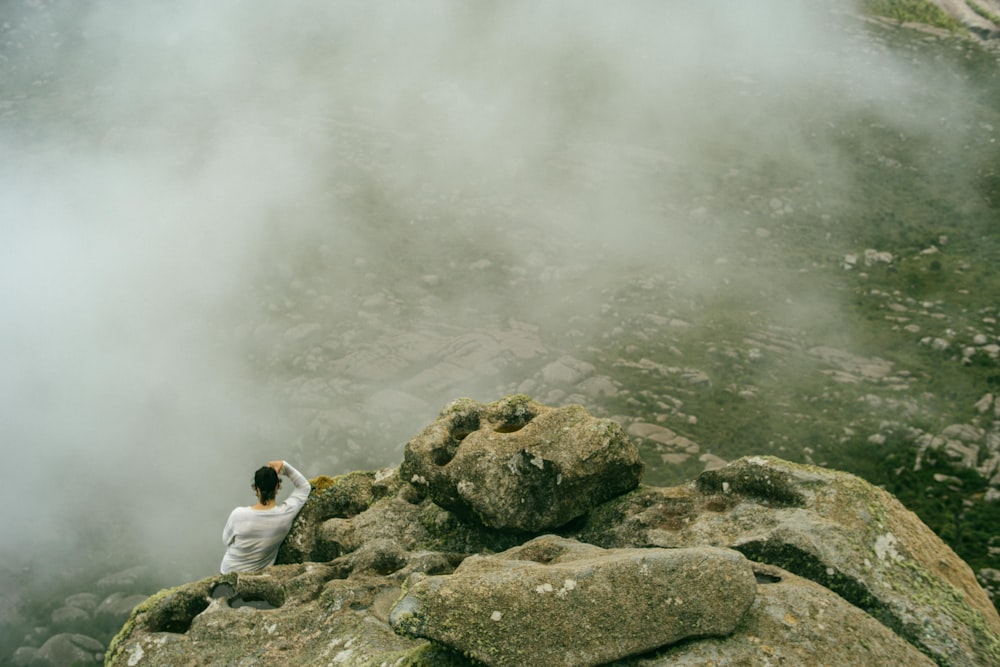 aerial photography of man sitting on peak of rock formation