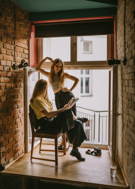 woman standing beside another woman sitting on chair