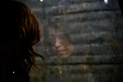 woman looking at the floor, face reflected in a window