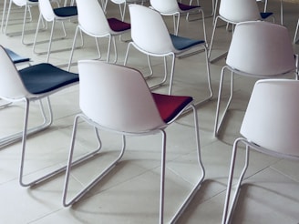Rows of modern chairs with white plastic backs and colored seats arranged neatly. The floor is made of light-colored tiles, creating a clean and organized atmosphere.