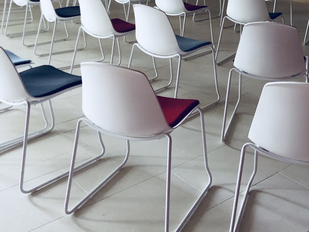 Rows of modern chairs with white plastic backs and colored seats arranged neatly. The floor is made of light-colored tiles, creating a clean and organized atmosphere.