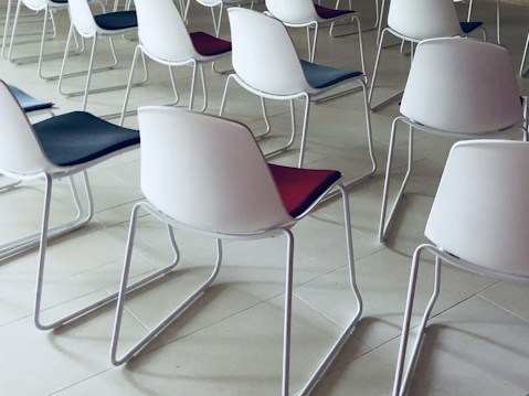 Rows of modern chairs with white plastic backs and colored seats arranged neatly. The floor is made of light-colored tiles, creating a clean and organized atmosphere.