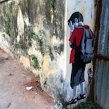 A piece of street art portraying a child leaning against an aged, weathered wall with patches of green foliage. The child is depicted in a stylized manner, wearing a red shirt and a backpack, with hands covering their face as if in sadness or distress. The wall and ground show signs of decay and neglect.